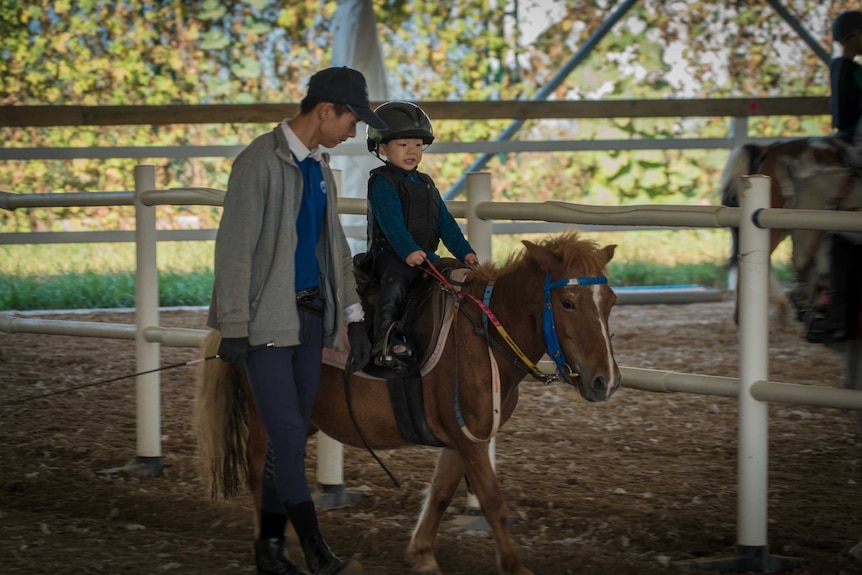 Duan Hui Ping walks alongside his son who is riding a pony.