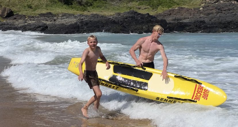two blonde teenagers in surf holding life saving paddle board