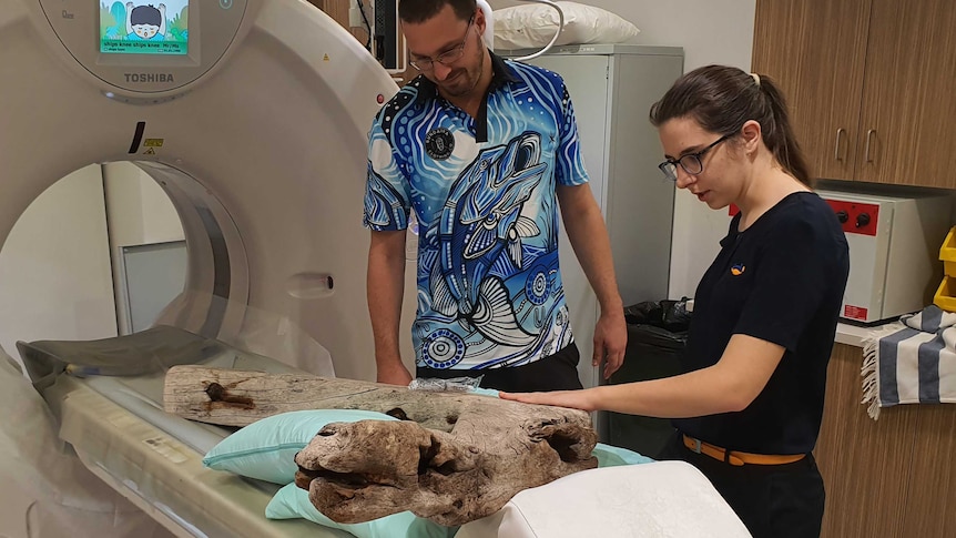 male and female radiologists in lab with long piece of wood in CT scanner