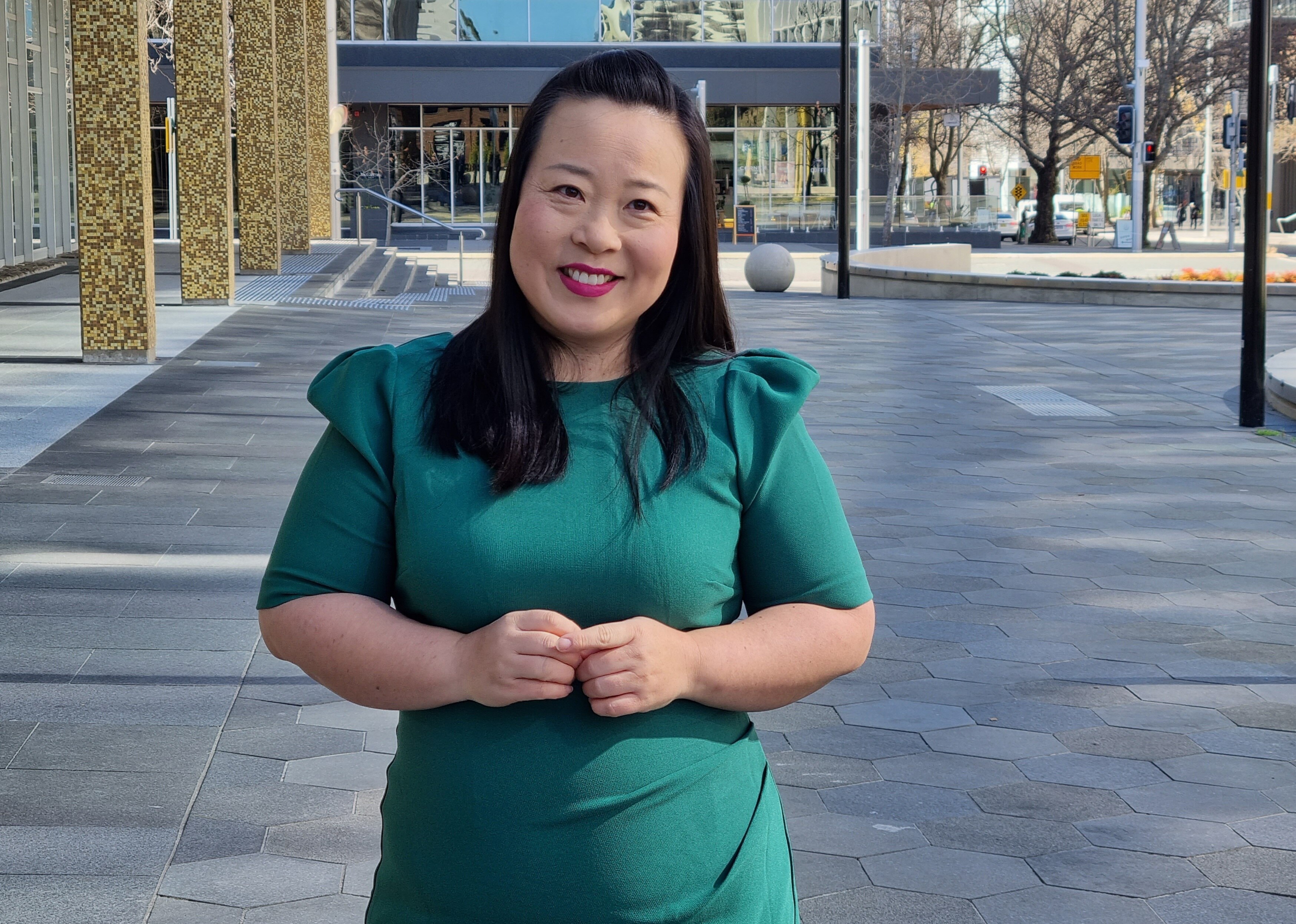 A woman with black hair wearing a teal dress smiles.