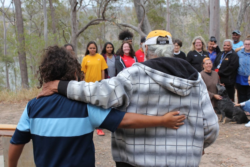 A man with grey hair and a young person with curly black hair walk arm in arm towards a group of people.