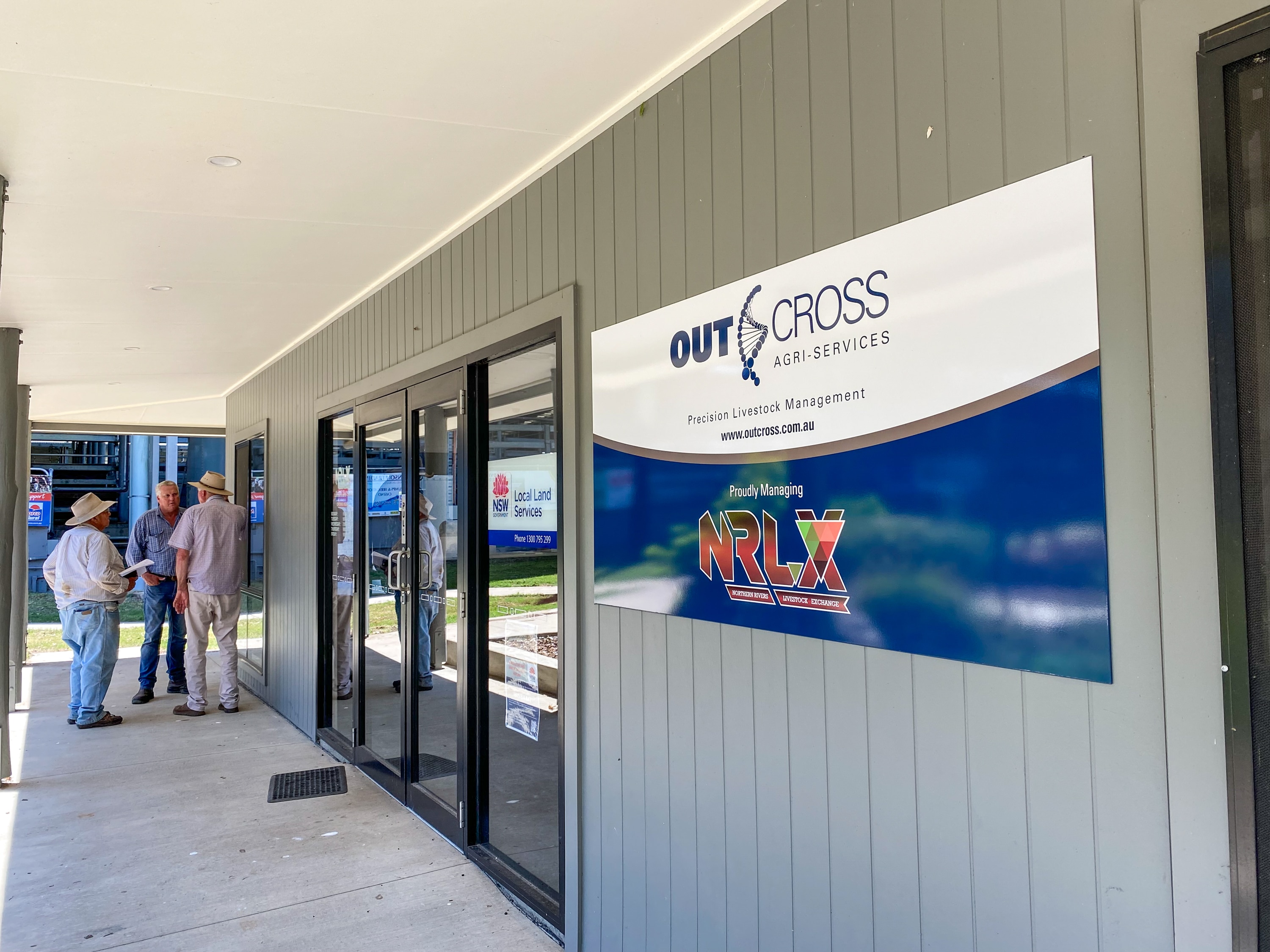 Three producers stand outside an office at a saleyard.