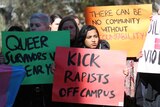 Protesters hold up signs reading 'Kick rapists off campus' and 'There can be no community without accountability'