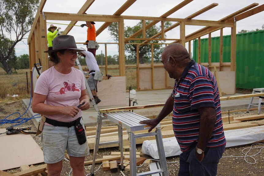 A woman and man smile to each other as a shed is constructed behind them