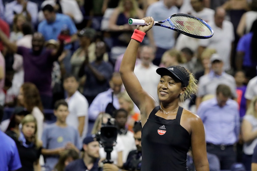 A female tennis player wearing black waves her racquet at the crowd