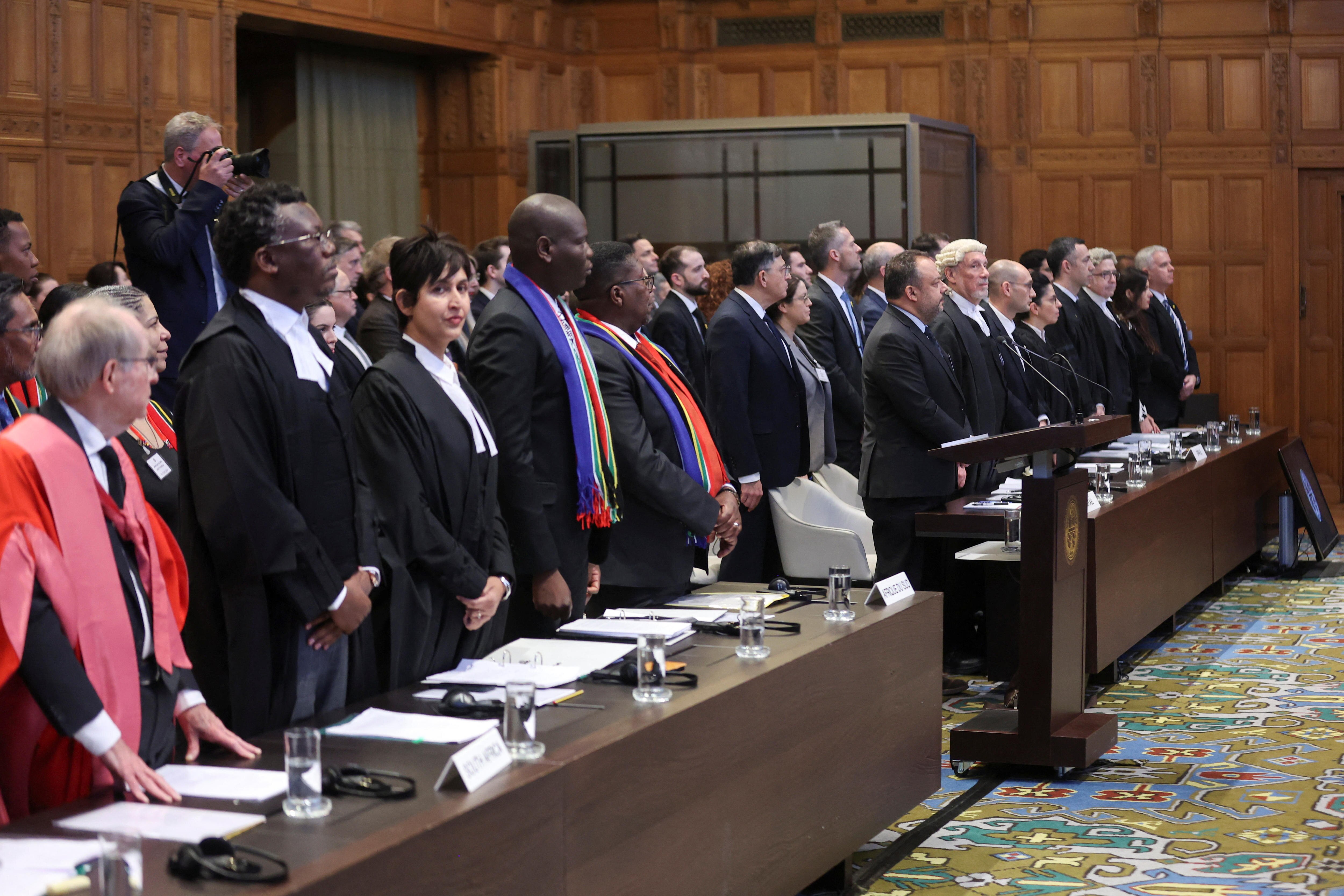 A group of people stand before desks covered in paper in large room, facing fowards. One person, Adila Hassim, faces the camera.