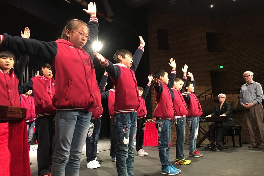 Chinese students on stage performing without instruments, in unison.