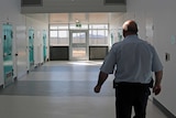 Prison guard walks along corridor past cells
