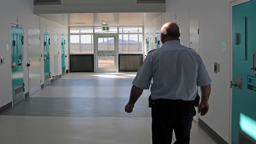 Prison guard walks along corridor past cells