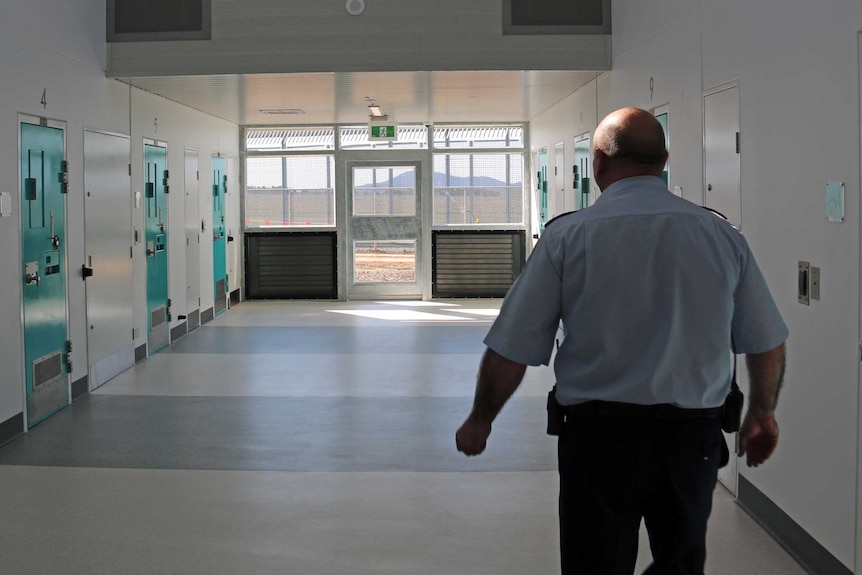 Prison guard walks along corridor past cells