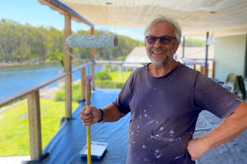 Man with a paint roller covered in white paint splats.