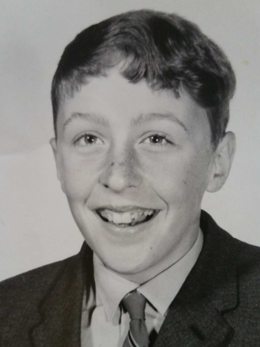 A boy dressed in a school uniform smiles in a black and white photo.