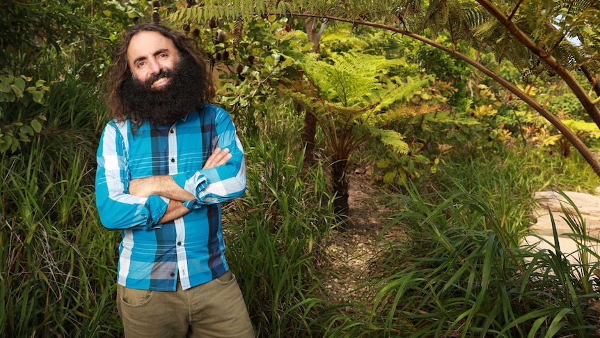 Costa Georgiadis standing in front of some trees in a red button-up shirt.