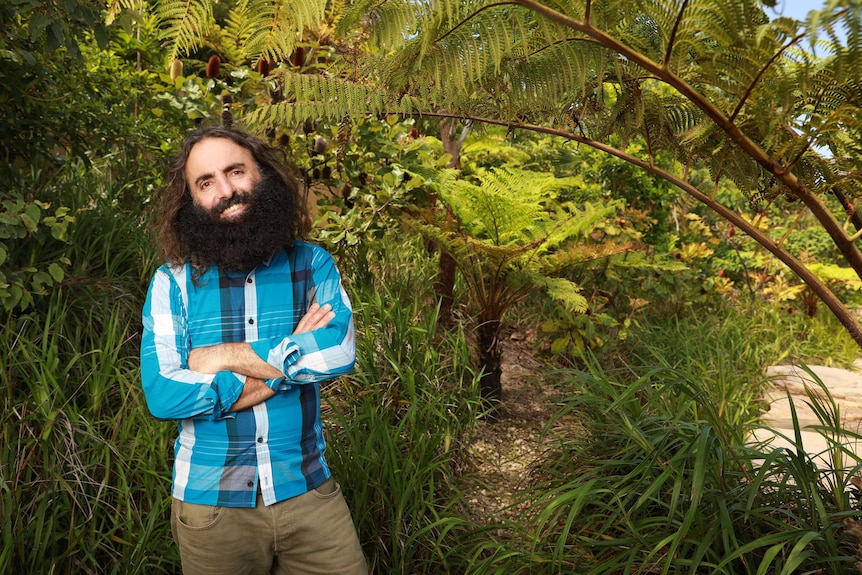 Costa Georgiadis standing in front of some trees in a red button-up shirt.