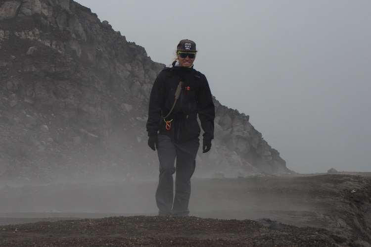 A heavily-clothed man walks through steam in a bleak, rocky landscape.