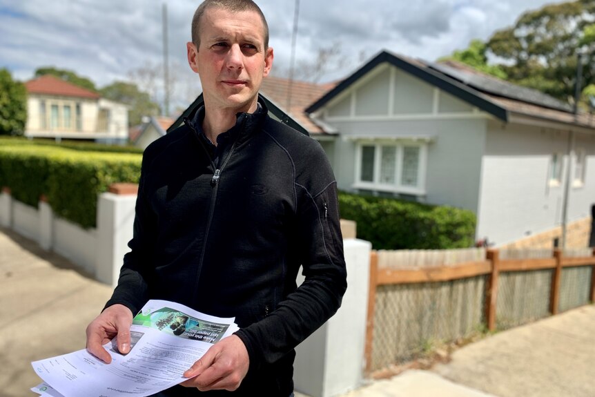 a man outside a house with energy bills in his hand looking unimpressed