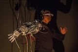 Stelarc wears a mask, headphones and a robotic arm in his exhibit at Radical ecologies.