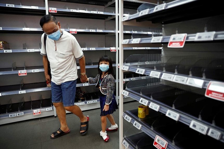 A man and child wearing masks walk past empty shelves.