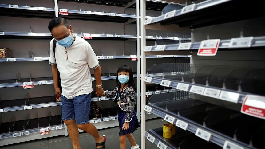 A man and child wearing masks walk past empty shelves.