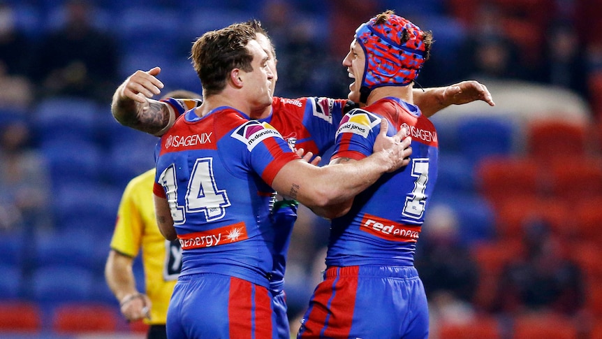 Three Newcastle Knights NRL players embrace as they celebrate a try.