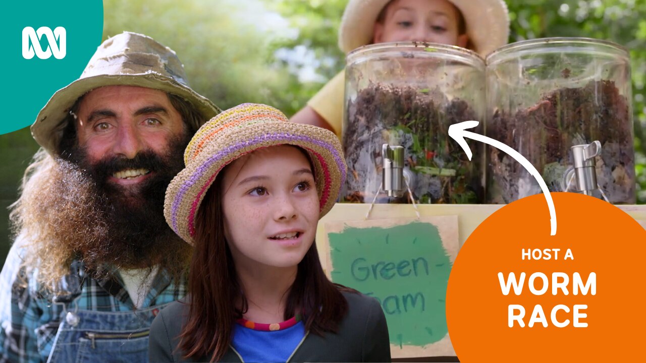 A man with a bushy beard and two girls gather around two transparent worm farms.