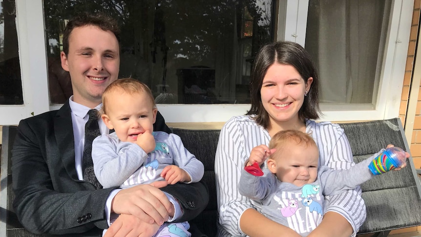 Sam Castleman and Karlie McRitchie sitting on a sofa on their front verandah holding their twin daughters