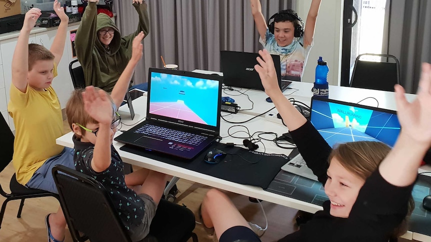 Group of autistic children around table with hands in the air excited to be learning gaming skills