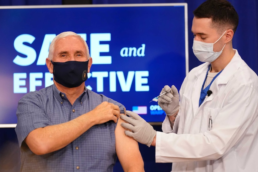 Un homme en chemise bleue reçoit une injection d'un homme en blouse blanche.