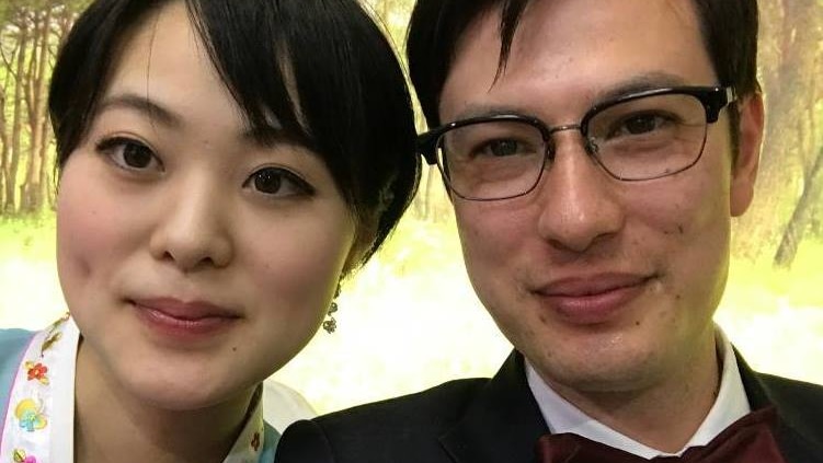 A selfie of a smiling man and woman with a forest in the background.