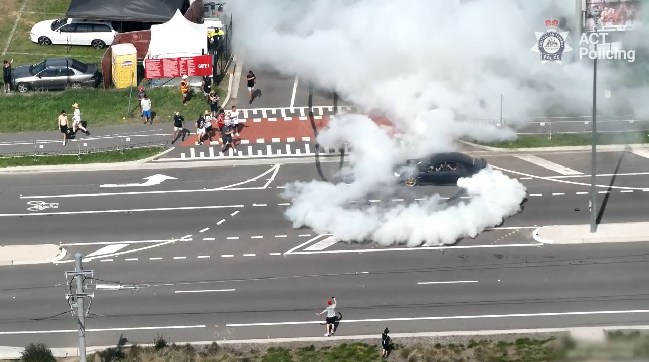 A black car does a burnout within metres of people.