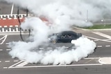 A black car does a burnout within metres of people.