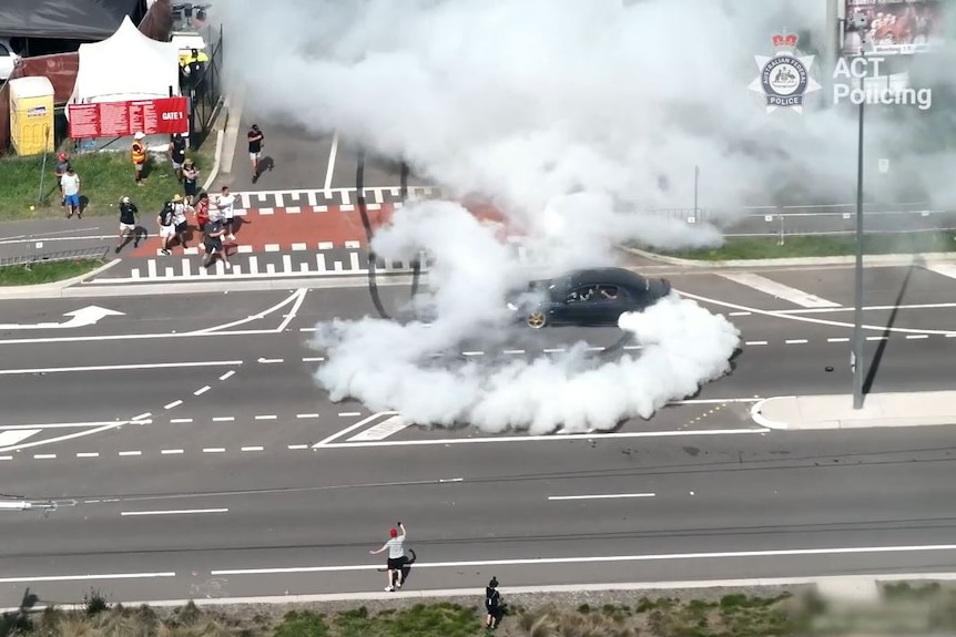 A black car does a burnout within metres of people.