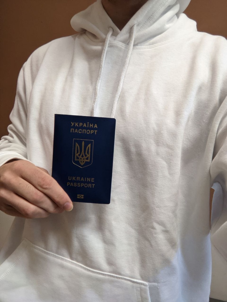 A man in white hoody holding a blue Ukraine passport.