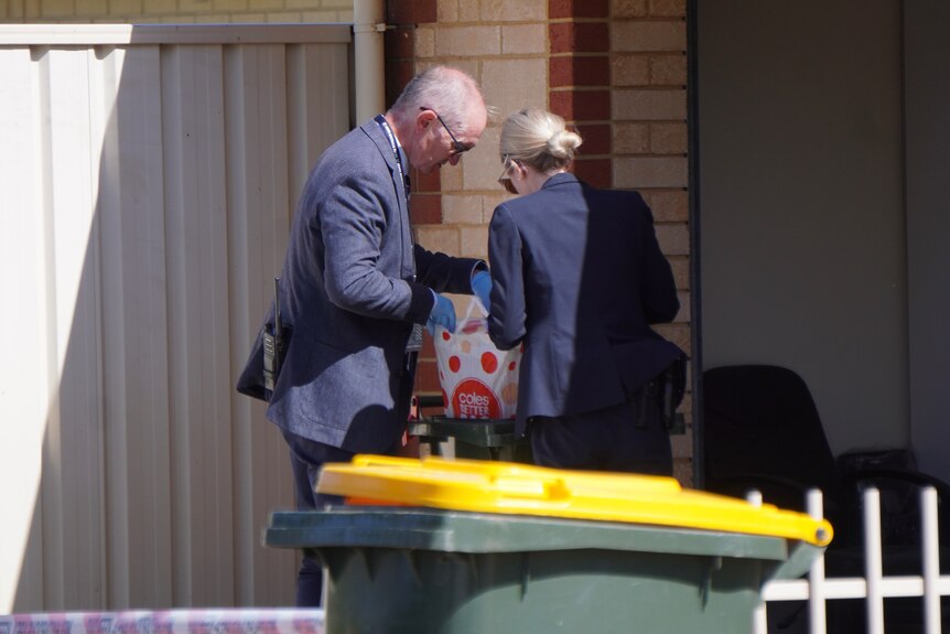 A man and a woman wearing blue suits look at a Coles shopping bag in a bin