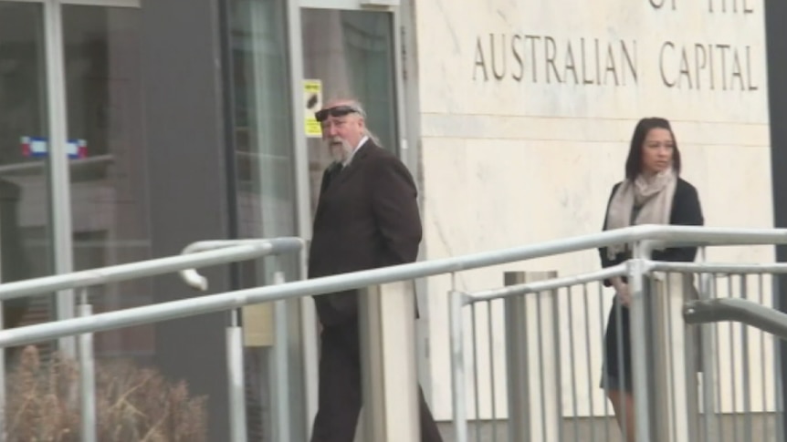 A man with a grey handlebar moustache and wearing sunglasses on his head walks into the court building.