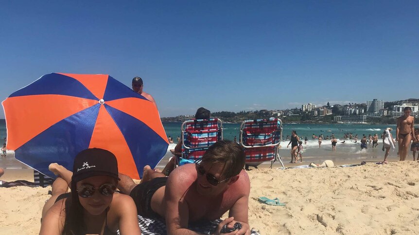 A man and woman lying on the sand try to keep cool at Bondi Beach in Sydney