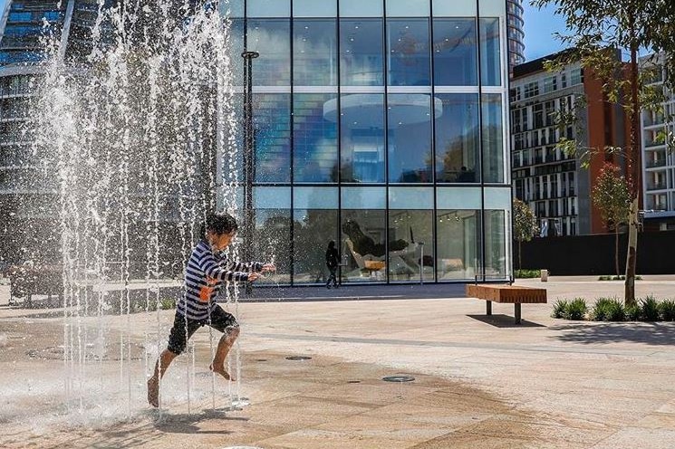 A fully clothed child runs through a fountain on a hot day