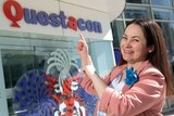A woman points at the Questacon sign, smiling.