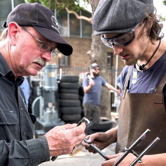 Two men examine blacksmith tools.