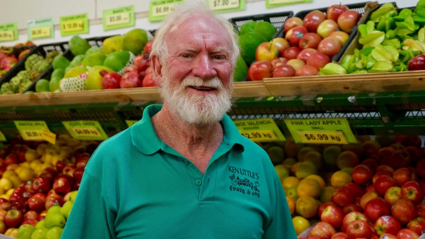 An older man stands in a store in front of fruit and vegetables.