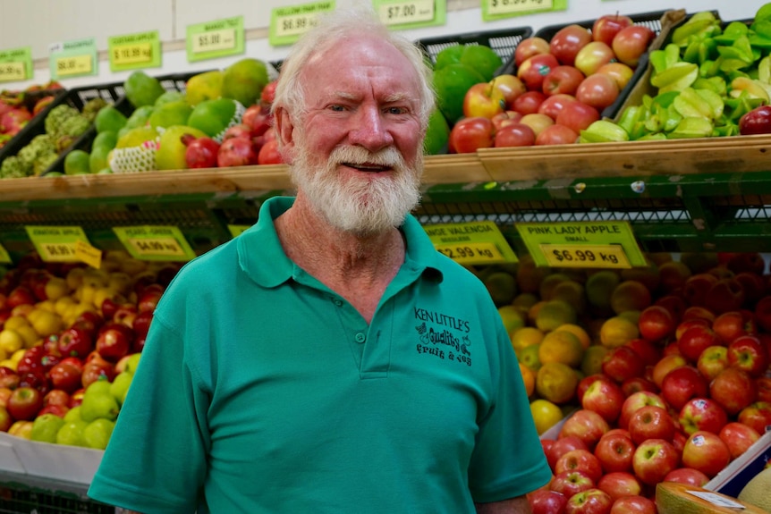 An older man stands in a store in front of fruit and vegetables.