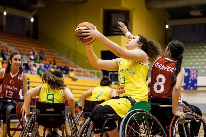 Annabelle Lindsay holds a basketball above her head while sitting in a wheelchair.
