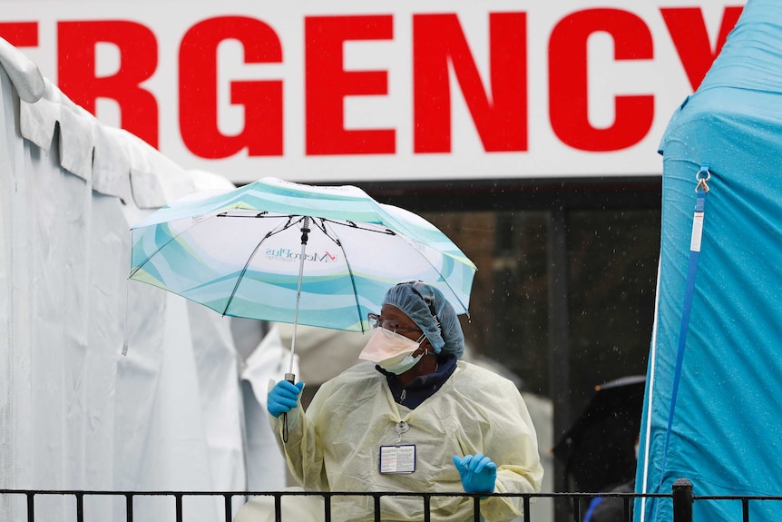 Person wearing protective clothing holds an umbrella over their head.