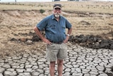 A man stands with his hands on his hips on a dry, cracked patch of land.