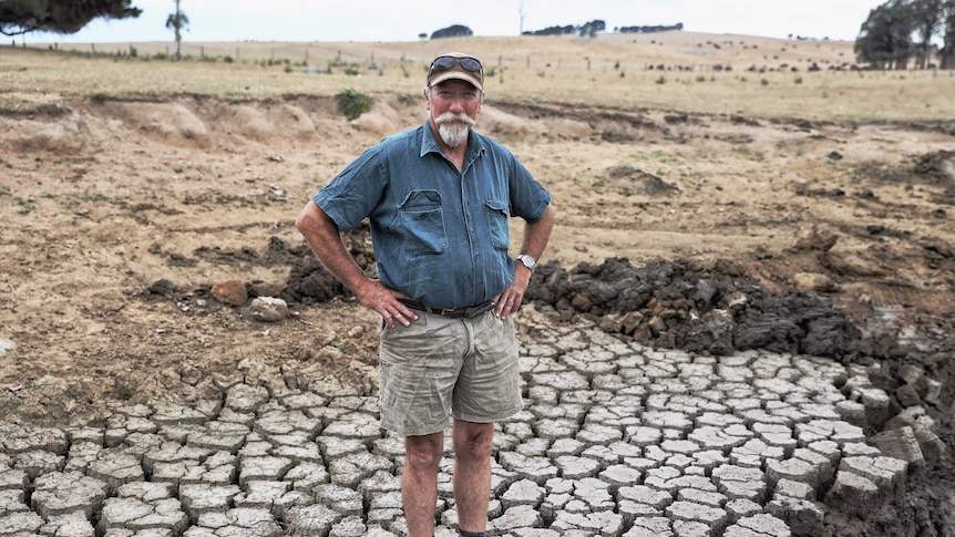 A man stands with his hands on his hips on a dry, cracked patch of land.