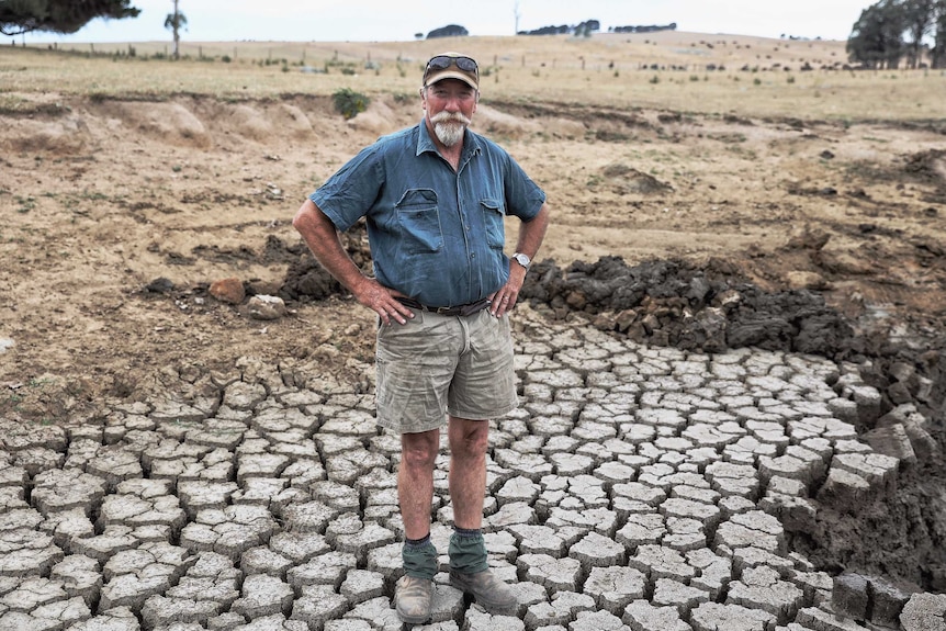 A man stands with his hands on his hips on a dry, cracked patch of land.