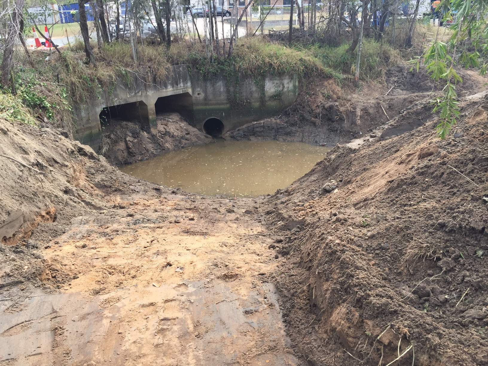 Large hole partially filled with water next to a drain
