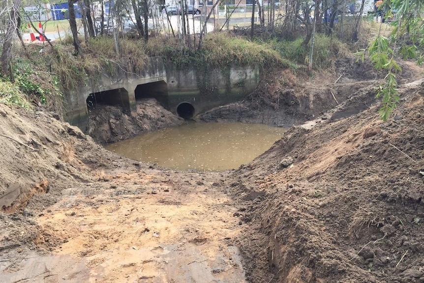 Large hole partially filled with water next to a drain