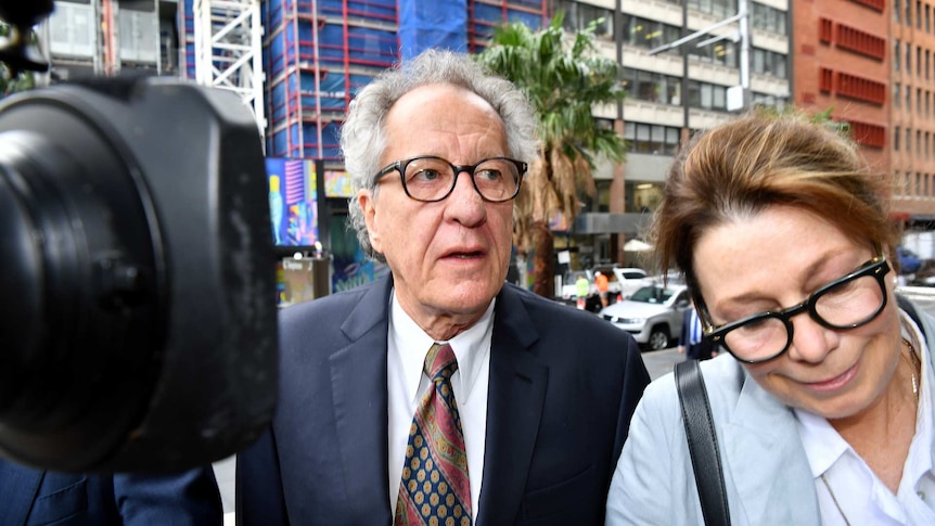 Geoffrey Rush and a female with a camera lens to the right outside court