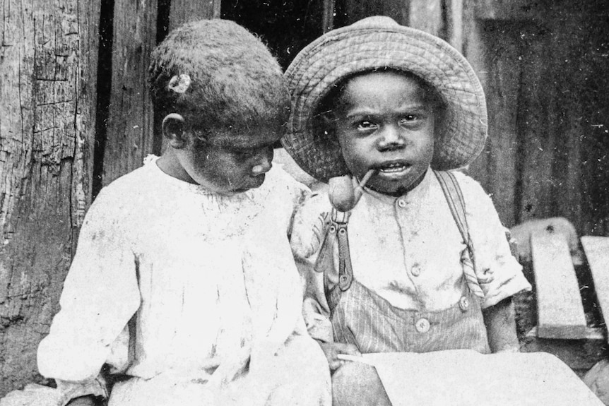 Black and white historical shot of two south sea islander small children posing. One has a pipe in his mouth.